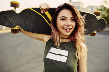 Beautiful young tattooed woman with his longboard on the road in the city in sunny weather