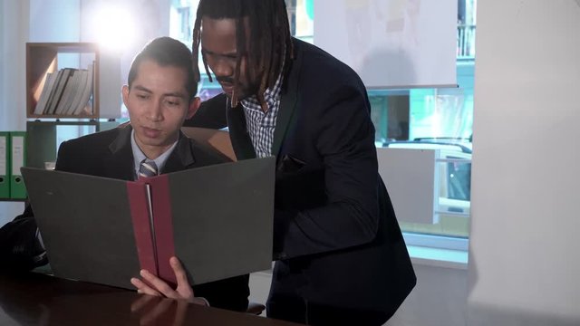 Asian and African American office workers reading paper documents at workplace