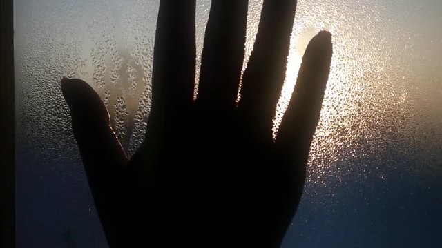 female hand in the foreground wipes the drops of water from the glass on a background of a beautiful sunset and the sky. 1920x1080