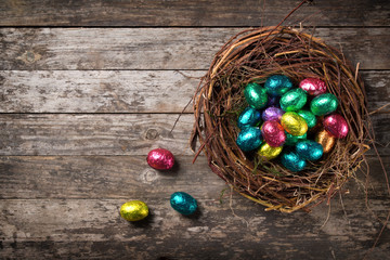 Chocolate easter eggs wrapped in colorful foil in the nest on wooden background, top view