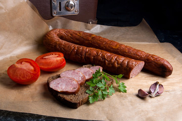Slices of smoked sausage with spice, herbs and vegetables on the packaging paper.