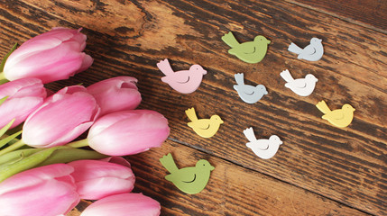 Rosa Tulpen mit kleinen bunten Vögeln auf rustikalem Holztisch 