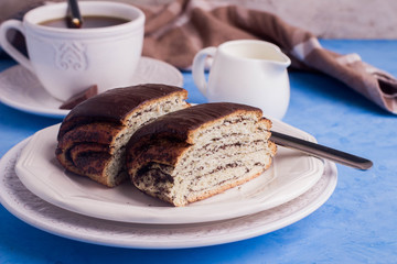 Homemade pastry with poppy seeds for breakfast icing chocolate on white plate with cup of coffee and milk on blue table background. copy space. 