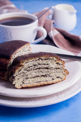 Homemade pastry with poppy seeds for breakfast icing chocolate on white plate with cup of coffee and milk on blue table background. copy space. 