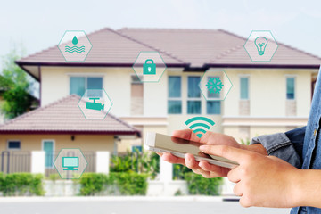 Hand using smart phone as smart home control application over blurred house background, smart home...