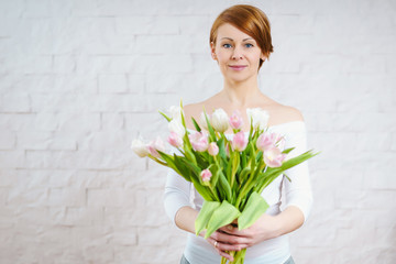 beautiful woman holding a bouquet of white and pink tulips on a light background