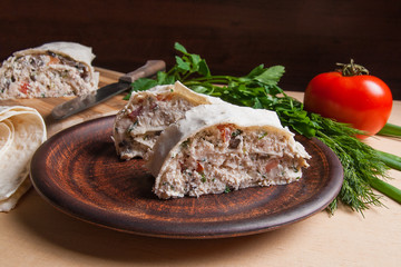Two pieces of pita bread or lavash roll with cottage cheese or curd, chicken, tomatoes and herbs - dill, onion, parsley on brown clay plate..