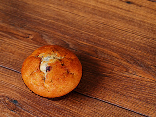 Single blue berry muffin on a wooden surface.