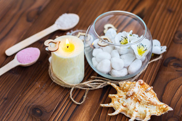White stones in a glass vase, flowers and a big candle on a dark wooden background for spa and relaxation
