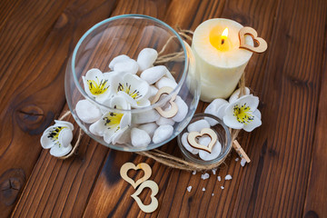 White stones in a glass vase, flowers and a big candle on a dark wooden background for spa and relaxation