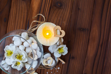 Obraz na płótnie Canvas White stones in a glass vase, flowers and a big candle on a dark wooden background for spa and relaxation