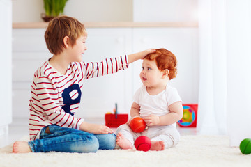 cheerful senior kid playing with his junior toddler brother at home