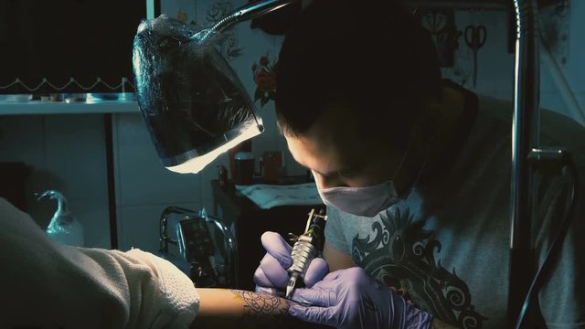Tattoo master in gloves does tattoo on hand