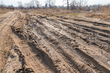 Deep tires tracks on the road covered by wet muddy sand