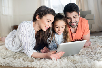 Fototapeta premium Happy family with one child lying on carpet and using digital tablet