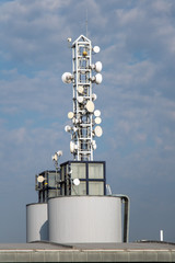 Telecommunication mast with microwave link on top roof at blue sky background.
