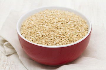 raw rice in red bowl on wooden background