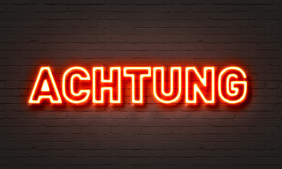 Achtung neon sign on brick wall background.