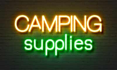 Camping supplies neon sign on brick wall background.