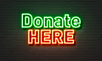 Fototapeta premium Donate here neon sign on brick wall background.