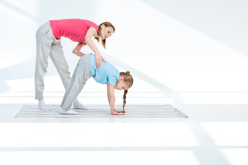 Happy young mother exercising with daughter on yoga mat