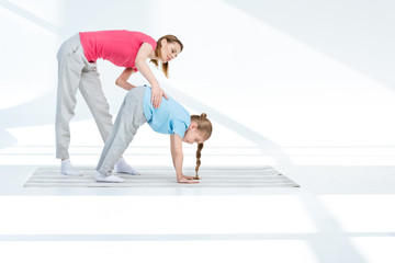 Obraz premium Happy young mother exercising with daughter on yoga mat