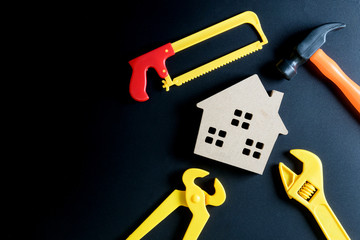 Wooden house toy and construction tools toy on black background with copy space.Home Repair concept, Repair maintenance concept, Renovation concept