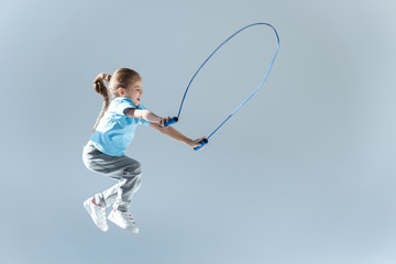 side view of happy girl humping exercising with skipping rope on grey - obrazy, fototapety, plakaty