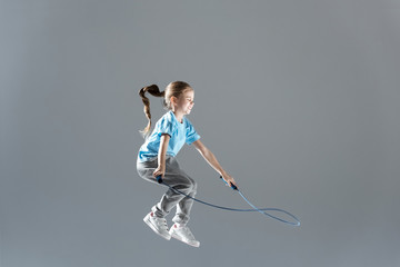 side view of happy girl humping exercising with skipping rope on grey - obrazy, fototapety, plakaty