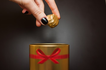 mano che tiene caramella di cioccolato della donna, tirato fuori da una scatola d'oro rotonda con un fiocco rosso su sfondo nero