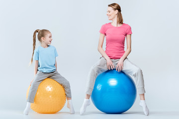 mother and daughter exercising with fitness balls on white