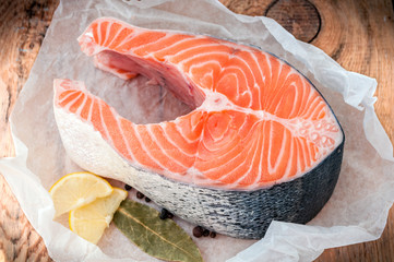 Raw salmon fish steak with lemon and spices on wooden rustic background. Cooking fish. Top view