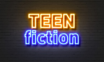 Teen fiction neon sign on brick wall background.