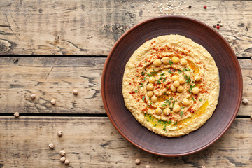 Hummus traditional Lebanese homemade chickpea vegan natural nutrition dip paste with paprika tahini parsley and olive oil in clay plate on rustic flat lay. Healthy dietary fiber protein food