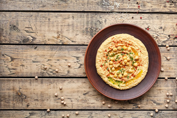 Hummus traditional homemade Mediterranean chickpea vegan natural nutrition dip paste with paprika tahini parsley and olive oil in clay plate on rustic flat lay. Healthy dietary fiber protein food