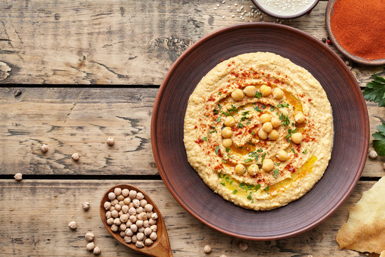 Hummus traditional homemade chickpea vegan natural nutrition lunch dip paste with pita bread paprika tahini parsley and olive oil in clay plate on rustic flat lay. Healthy dietary fiber protein food
