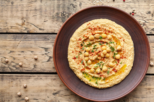 Hummus traditional homemade chickpea vegan natural nutrition dip paste with paprika tahini parsley and olive oil in clay plate on rustic flat lay. Healthy dietary fiber protein food