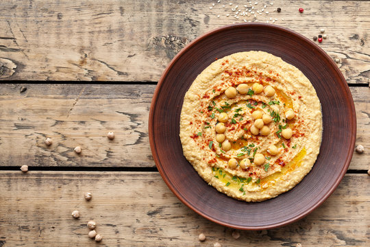 Hummus traditional Lebanese homemade chickpea vegan natural nutrition dip paste with paprika tahini parsley and olive oil in clay plate on rustic flat lay. Healthy dietary fiber protein food