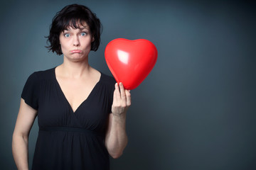 Beautiful Woman, holding a Red Heart Balloon, on Grey Background with Copy Space