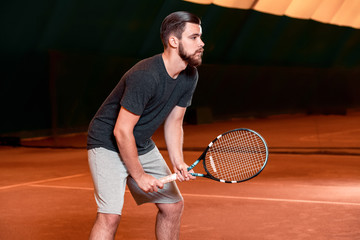 Handsome young man in t-shirt holding tennis racket on tennis court