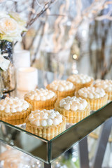 Cupcakes with white cream on the table decorated with white flowers and candles