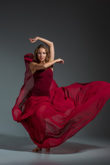 Young beautiful dancer in red dress posing on a dark gray studio background
