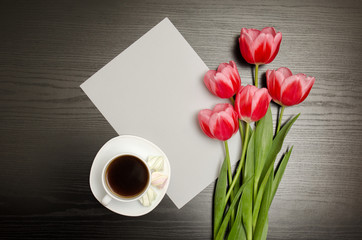 White blank sheet of paper, pink tulips and a mug of coffee. Black table. top view