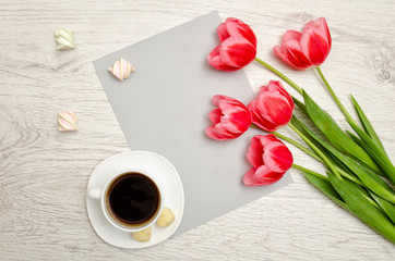 Fototapeta na wymiar Pink tulips on a blank sheet of paper, mug of coffee and marshmallows, light wooden background. top view, space for text