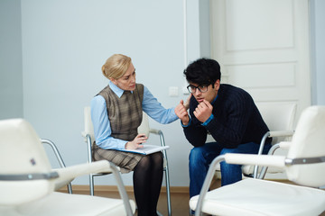 Portrait of young man opening up his problems to mental health doctor comforting him after support...
