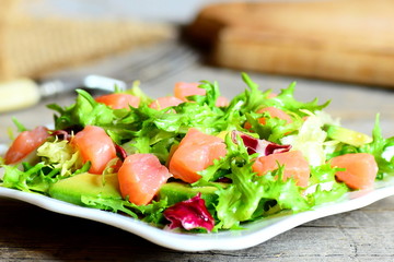 Delicious and simple salmon salad on a plate. Salad prepared with smoked salmon, salad mix and fresh avocado and dressing with olive oil and lemon juice. Vintage style. Closeup
