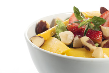 A healthy fresh salad of green lettuce with nuts, mango, strawberry, tomatoes in a white bowl isolated over white background.