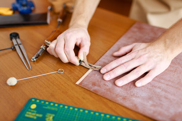 Hands of upholsterer processing leather workpiece
