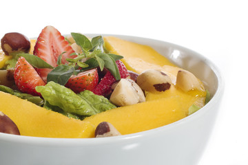 A healthy fresh salad of green lettuce with nuts, mango, strawberry, tomatoes in a white bowl isolated over white background.