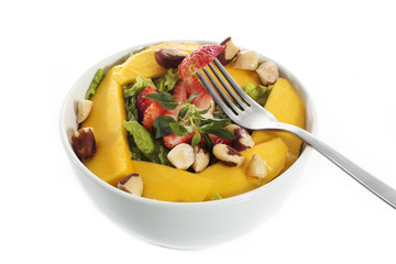 A healthy fresh salad of green lettuce with nuts, mango, strawberry, tomatoes in a white bowl isolated over white background.
